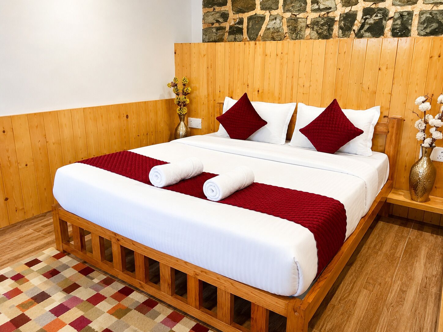 Una cama con estructura de madera, ropa de cama blanca, almohadas rojas y blancas, y una manta roja.