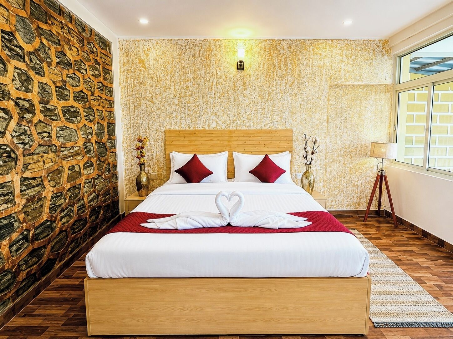 A hotel room with a large bed, a stone wall, a wooden headboard, and a window with a view.