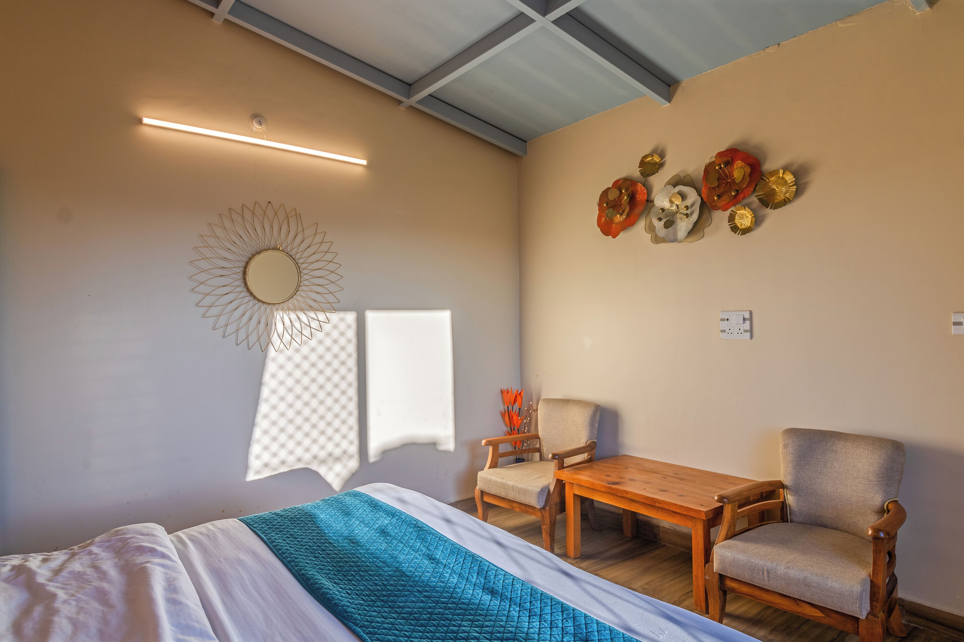 A hotel room with a bed, two chairs, a wooden table, a mirror, and wall decorations.