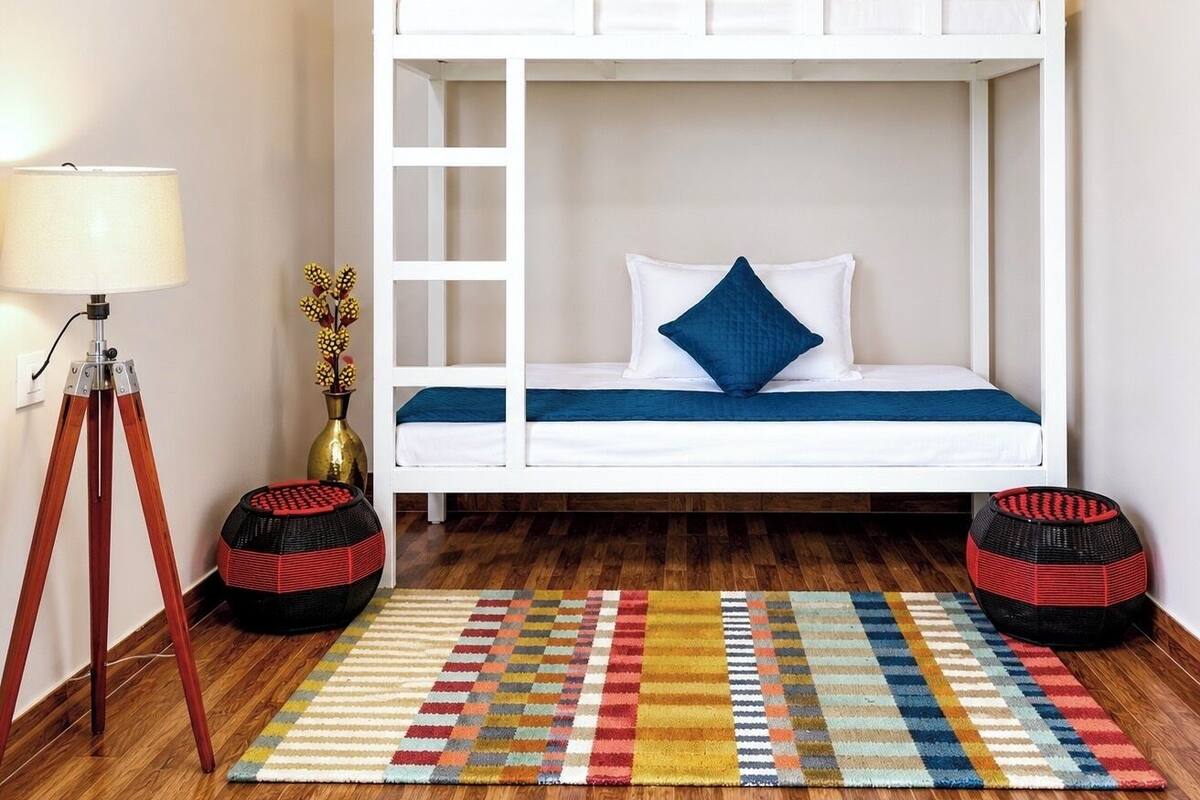 A bunk bed room with a wooden floor, a colorful rug, a lamp, and a small table with a vase.