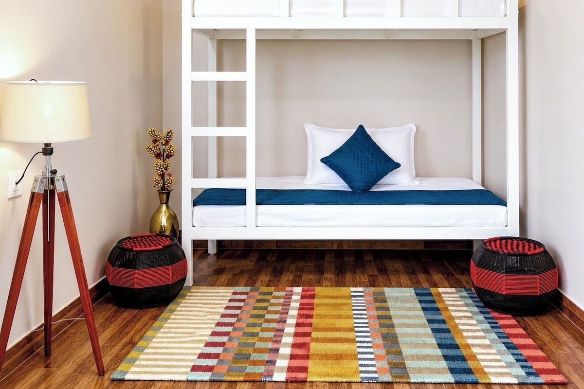 Une chambre avec un lit superposé, un plancher en bois, un tapis coloré, une lampe et une petite table sur laquelle se trouve un vase.