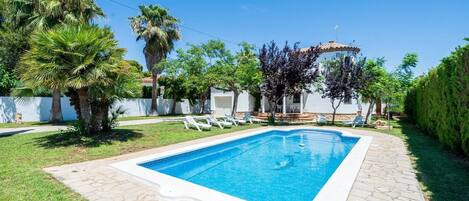 A rectangular swimming pool with a tiled edge, surrounded by a stone patio.