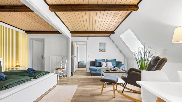 Ein modernes Loft mit freiliegenden Holzbalken, einem Schlafsofa, einem Schaukelstuhl und einem Essbereich.