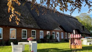 Ein Haus mit Strohdach und Backsteinfassade, einer weißen Tür und einem kleinen Garten mit Tisch und Stühlen.