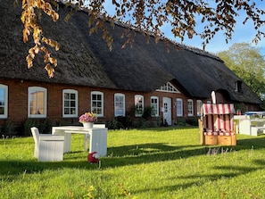 Ein Haus mit Strohdach und Backsteinfassade, einer weißen Tür und einem kleinen Garten mit Tisch und Stühlen.