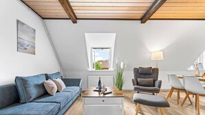 Ein modernes Wohnzimmer mit einem blauen Sofa, einem Holztisch, einem grauen Sessel und einem Essbereich mit weißen Stühlen.