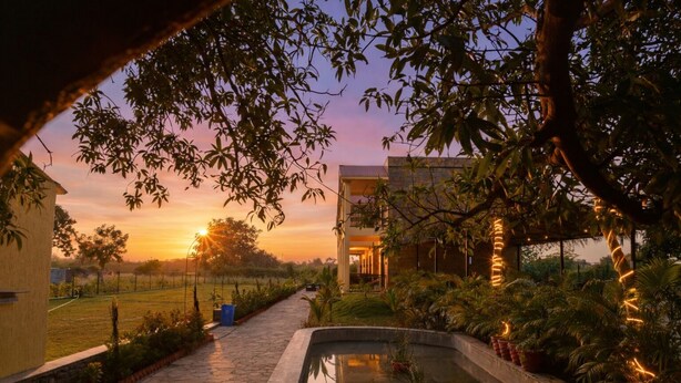 A serene outdoor setting with a pathway leading to a building, surrounded by lush greenery and a small water feature. - Achal Bagh – Boutique Stay Abu Road (Abu Road)