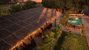 A thatched-roof structure with a pool and palm trees. - Achal Bagh – Boutique Stay Abu Road (Abu Road)