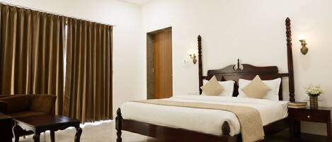 A neatly arranged bedroom with a large bed, a chair, a bedside table, and a door.