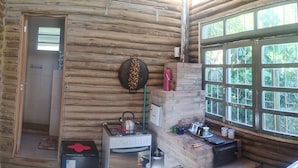 A log cabin interior with a gas stove, a refrigerator, a brick fireplace, and a large window. - Log cabin from Borussia, with heated bathtub. (Borussia)