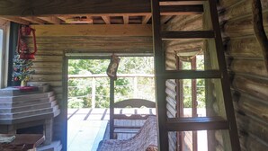 Une cabane avec une chambre à coucher située en mezzanine, une échelle en bois, un petit sapin de Noël et une vue sur l’extérieur.