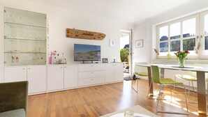 Eine moderne Küche mit Fernseher, weißen Schränken und einem Essbereich mit grünen Stühlen.