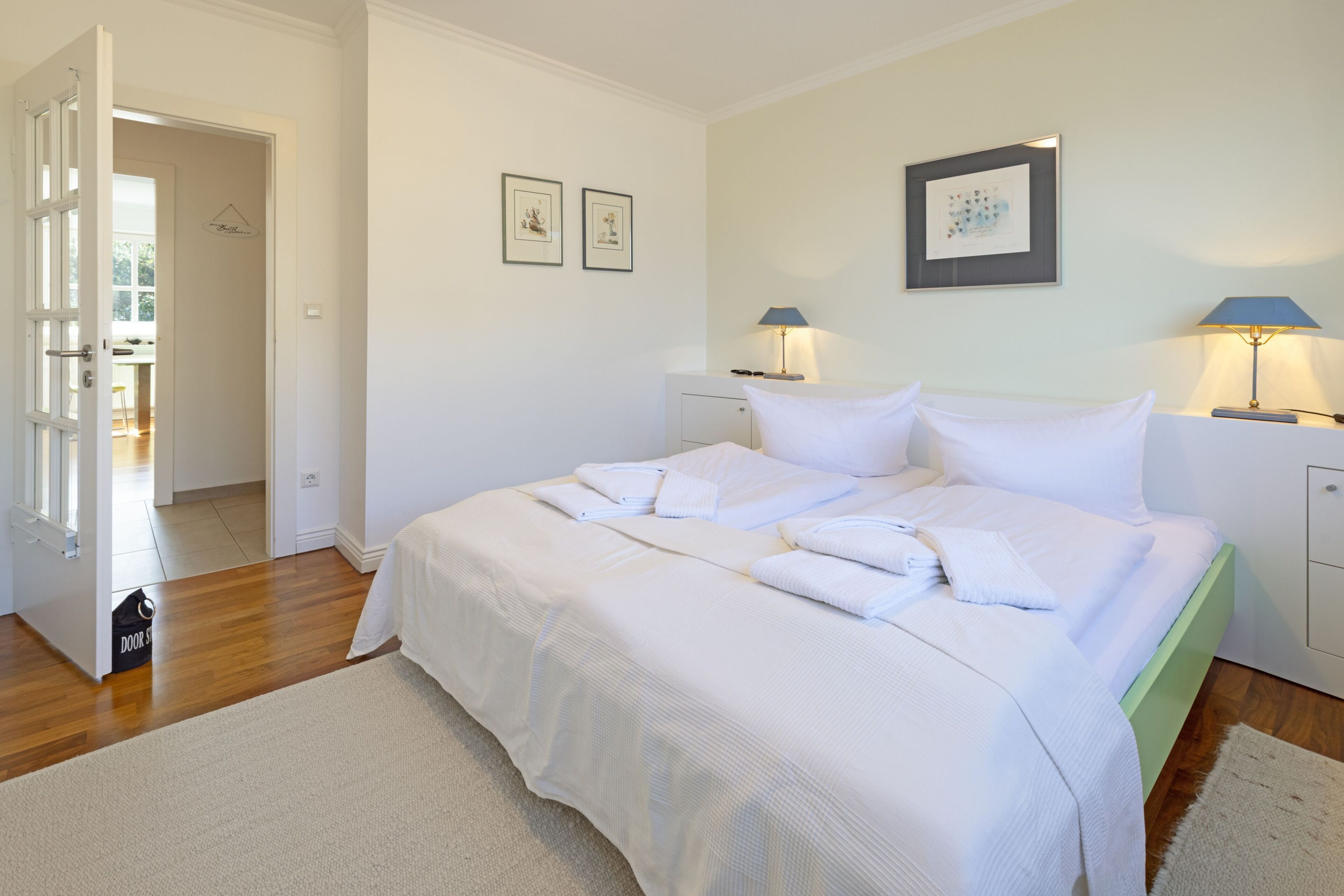 A neatly arranged bedroom with a bed, bedside tables, and a door leading to another room.