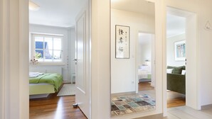 Ein Hotelzimmer mit Bett, Fenster, Tür und einem Flur, der zu einem anderen Zimmer führt.