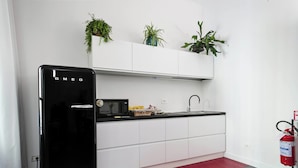 A modern kitchen with white cabinets, a black refrigerator, a black countertop, and a red rug. There are three potted plants on the wall above the cabinets. - Guesthouse Delle Navi - Room 4 (Roma)