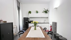 A dining area with a wooden table, chairs, a vase with flowers, a white table runner, a black refrigerator, a sink, and potted plants on the wall. - Guesthouse Delle Navi - Room 4 (Roma)