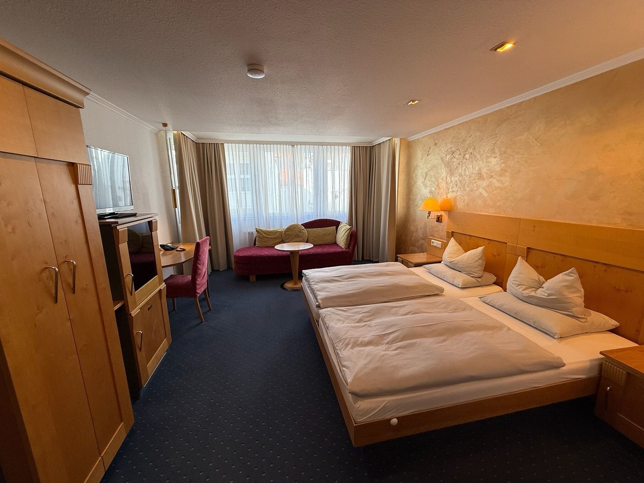 Ett hotellrum med en säng, ett skrivbord, en stol, en tv och ett fönster med gardiner.