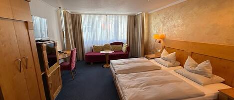 Ett hotellrum med en säng, ett skrivbord, en stol, en tv och ett fönster med gardiner.