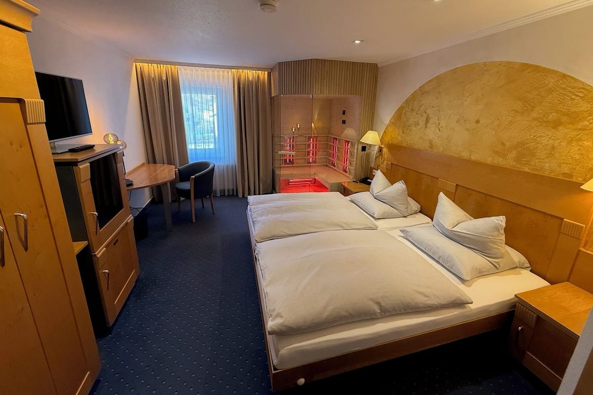 Habitación de hotel con cama, escritorio, silla, televisor y vistas al exterior.