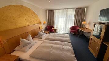Habitación de hotel con dos camas, un escritorio, una silla, un televisor y un ventanal con cortinas.