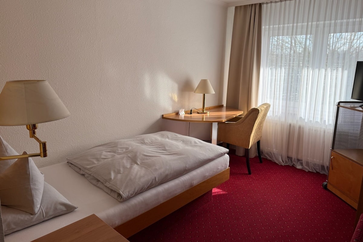Una habitación de hotel con cama, escritorio con lámpara, silla y televisor.