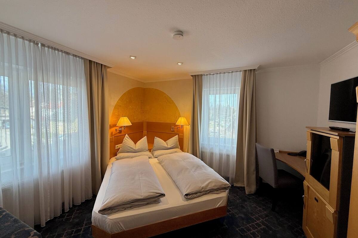 Habitación de hotel con una cama grande, dos lámparas de noche, un televisor y un escritorio.