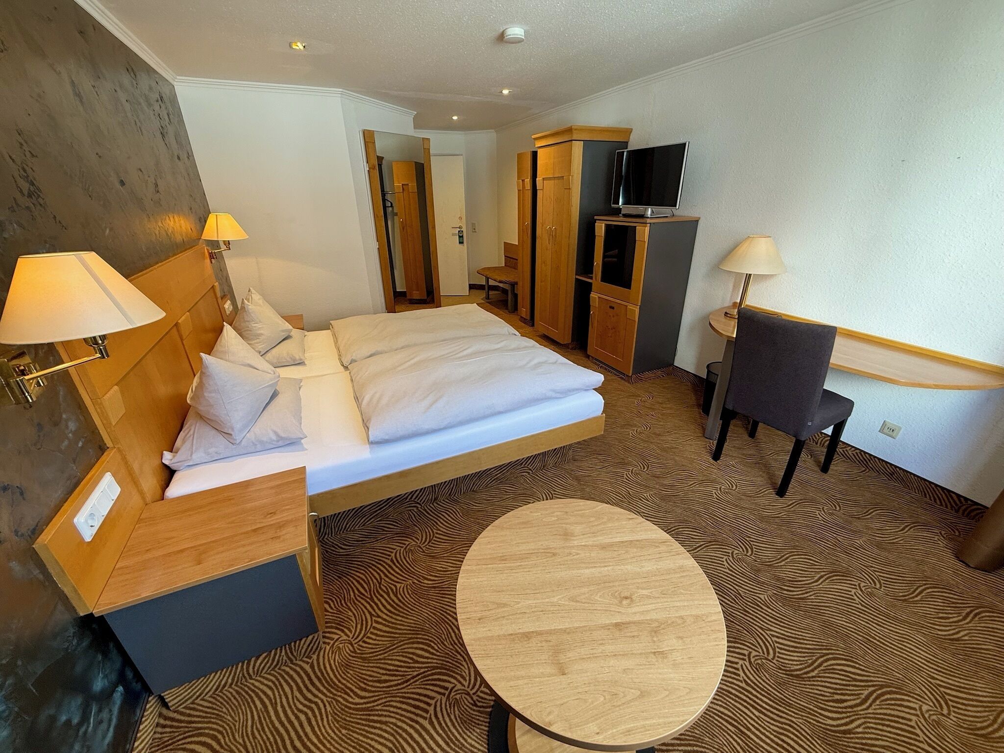Een hotelkamer met een bed, nachtlampjes, een televisie, een bureau en een stoel.