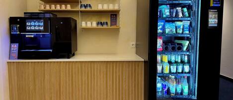 Máquina automática com diversas bebidas e petiscos, máquina de café, e uma prateleira com copos e um letreiro para KA BO coffee.