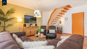 A living room with a sofa, armchair, coffee table, and a staircase.