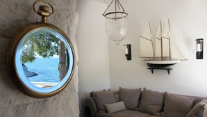 A living room with a round mirror reflecting a tree and water, a brown sofa, a hanging light fixture, and a model sailboat on the wall. - Seafront Villa Marella (Milna)