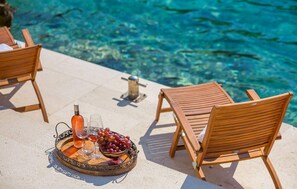 A poolside setting with wooden lounge chairs, a tray with a bottle, glasses, and grapes. - Seafront Villa Marella (Milna)