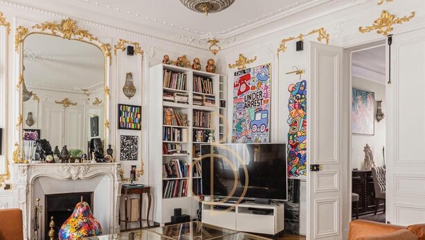 Uma sala de estar luxuosa com lareira, um espelho grande, estante de livros, televisão e um sofá moderno.