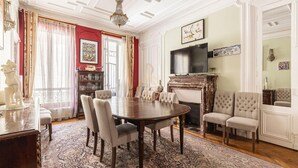 Uma sala de jantar formal com uma grande mesa redonda, várias cadeiras, uma lareira e uma televisão montada na parede.
