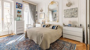 Quarto com uma cama grande, cômoda, espelho e lustre.