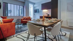 A modern living room with a sofa, chairs, and a dining table set for four. - Loft moderne 2BR - Cœur de Paris A/C portable (Paris)