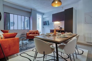 Ein modernes Wohnzimmer mit einer Couch, Sesseln und einem Esstisch für vier Personen.