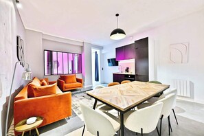 Ein modernes Wohnzimmer mit Essbereich, heller Beleuchtung und Blick zur Küche.