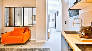 A modern kitchen with a wooden countertop, a sink, and a coffee machine. There is a bright orange chair and a large mirror on the wall. - Loft moderne 2BR - Cœur de Paris A/C portable (Paris)