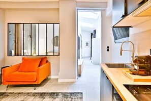 Eine moderne Küche mit einer Holzausziehtheke, einem Spülbecken und einer Kaffeemaschine. Ein leuchtend orangefarbener Stuhl und ein großer Spiegel sind an der Wand angebracht.