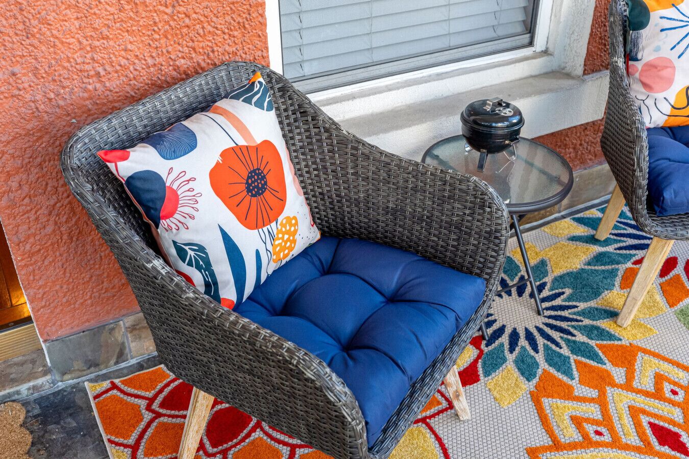 A wicker chair with a colorful floral pillow and blue cushion, placed on a patterned rug.
