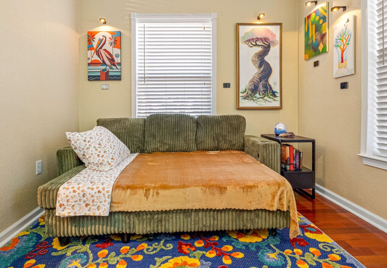 A bedroom with a bed, a window with blinds, a radiator, and artwork on the walls.