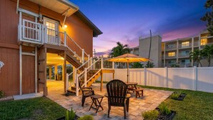 A patio area with outdoor furniture, a staircase, and a view of a building in the background. - Joe`s Beach House | Walk to IRB | Family Friendly (Indian Rocks Beach)