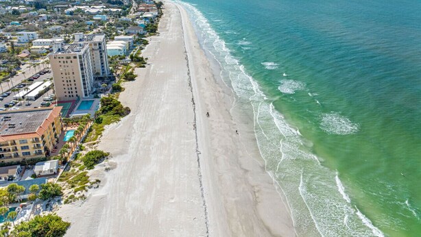 An aerial view of a coastal area with a long sandy beach, a hotel with multiple buildings, and a clear view of the ocean. - Joe`s Beach House | Walk to IRB | Family Friendly (Indian Rocks Beach)
