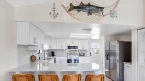 A modern kitchen with white cabinets, a large island with bar stools, stainless steel appliances, and nautical decor. - Joe`s Beach House | Walk to IRB | Family Friendly (Indian Rocks Beach)