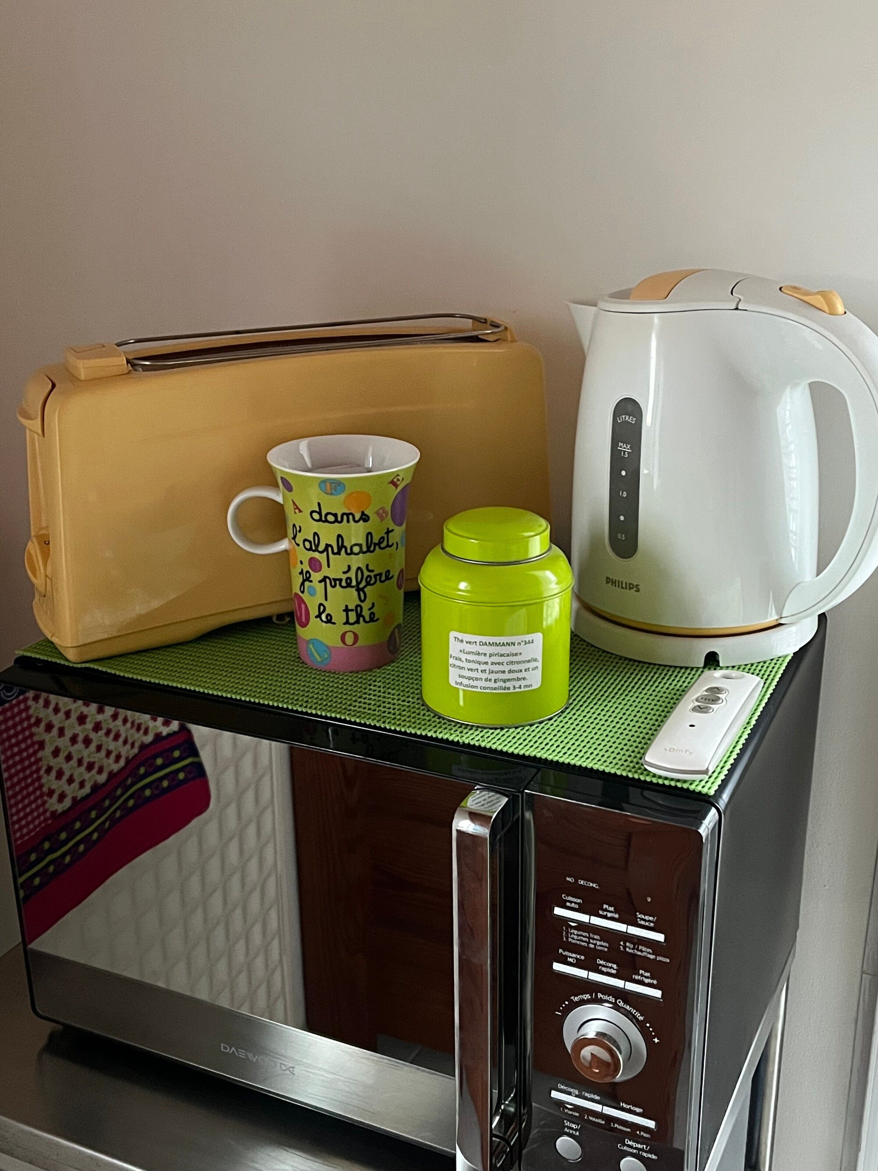 A microwave with a kettle, a mug, and a bottle on top.