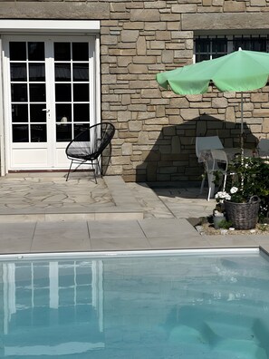 A stone building with a pool, a chair, and an umbrella. - La Marée Hôtes Guesthouse – Poolside Retreat (Piriac-sur-Mer)