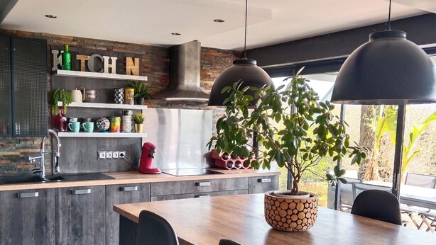 Une cuisine moderne avec un îlot central, des tabourets de bar noirs et une plante en pot.