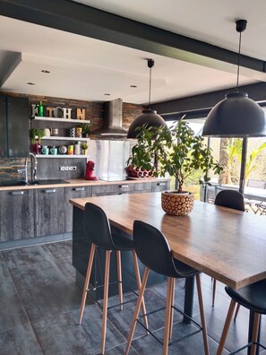A modern kitchen with a central island, black bar stools, and a potted plant. - Villa swimming pool urt (Urt)
