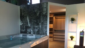 Une salle de bain moderne dotée d’un jacuzzi entouré de parois en verre, d’une fresque représentant un paysage urbain, d’une douche à l’italienne et d’une étagère intégrée où est posée une plante en pot.