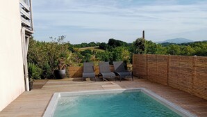 Une piscine rectangulaire dotée d’une terrasse en bois, entourée d’un mur en briques et agrémentée de plantes en pot.